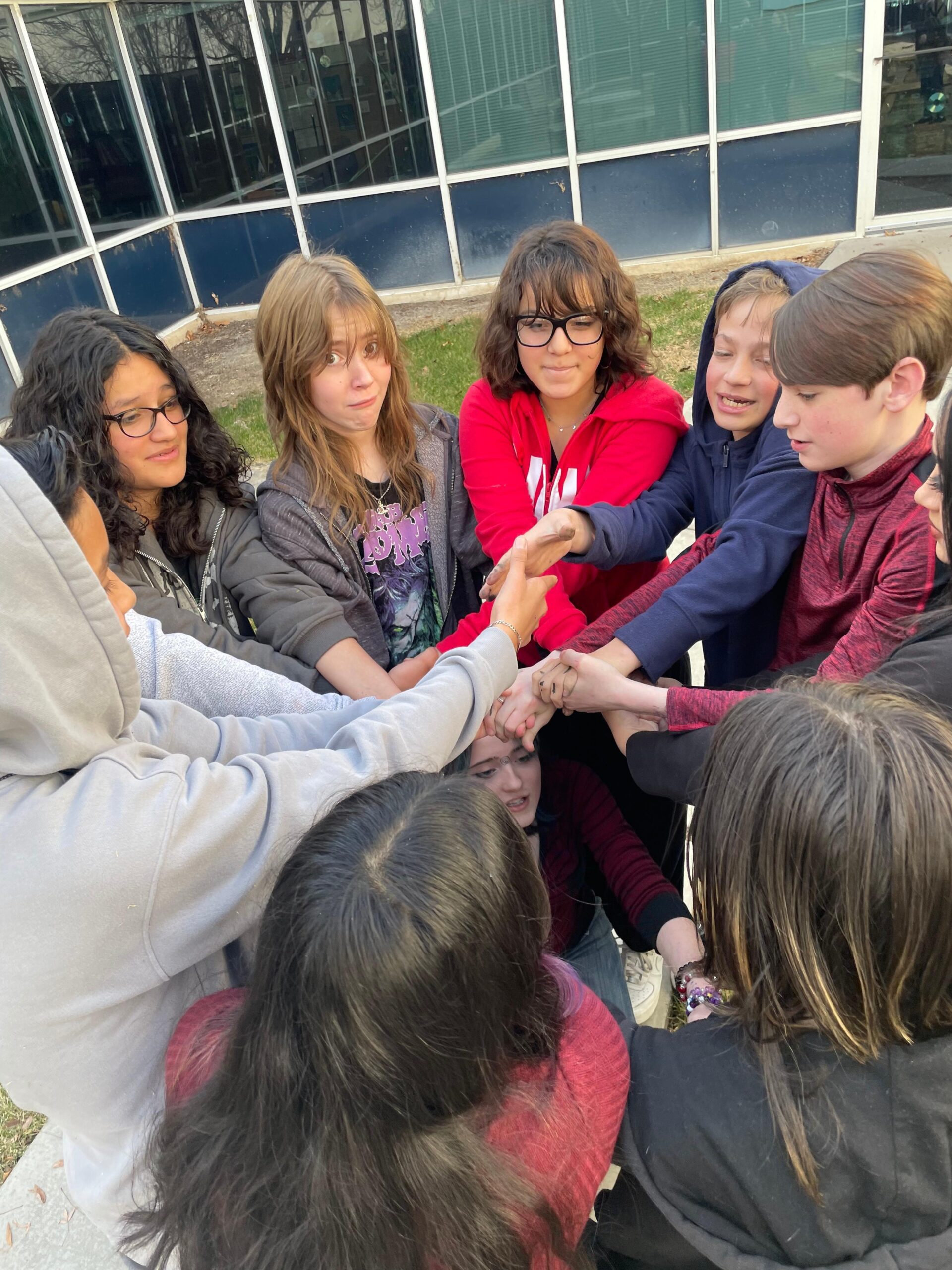 Students standing in a circle holding hands in the middle.